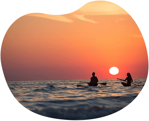Photo d'un couple sur des planches de surf, sur l'eau pendant un couché de soleil